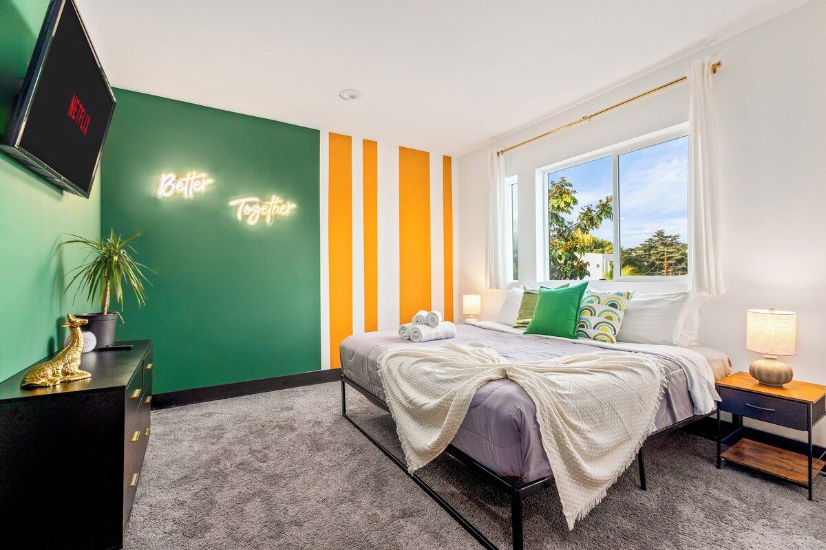 A modern bedroom with a bed, bedside tables, a TV, and a neon sign on the wall.
