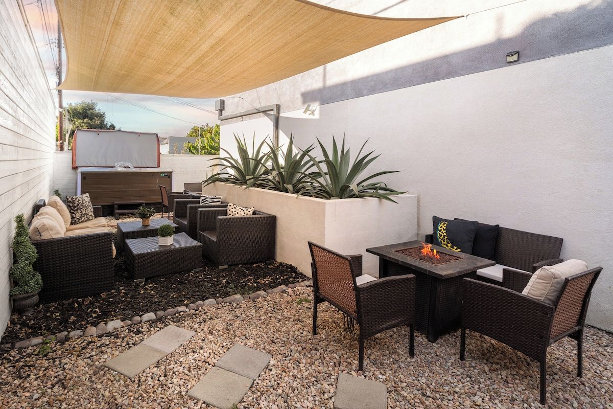 Een terras buiten met rieten meubilair, een vuurkorf en potplanten.