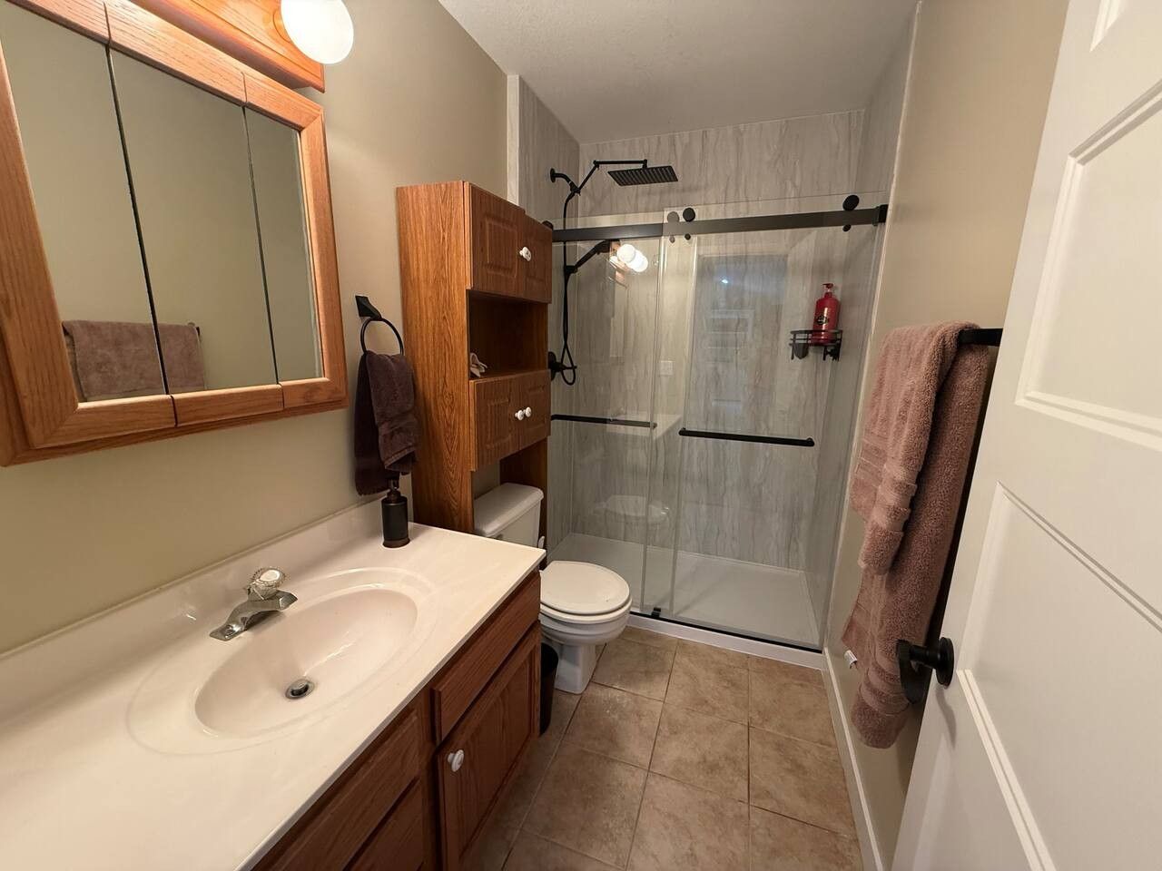 A bathroom with a sink, mirror, wooden cabinets, a toilet, and a glass-enclosed shower.
