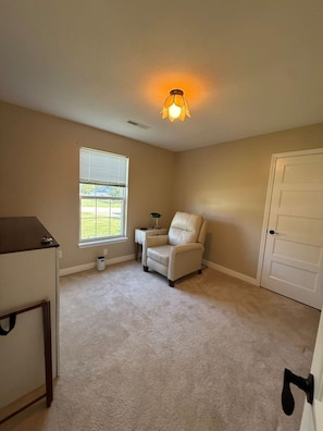 A room with a window, a chair, a desk, and a door.