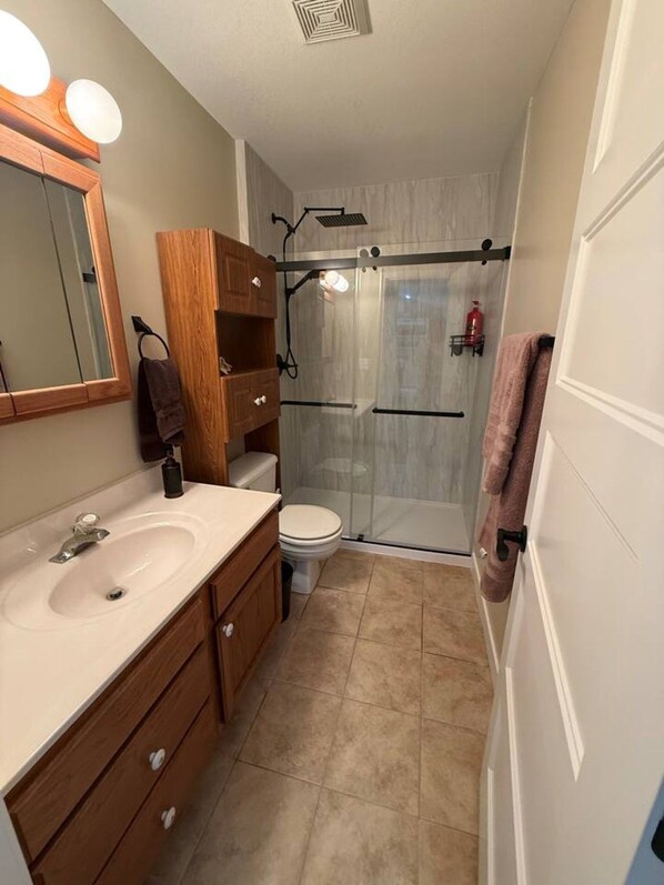 A bathroom with a sink, mirror, wooden cabinet, toilet, and a glass shower enclosure.