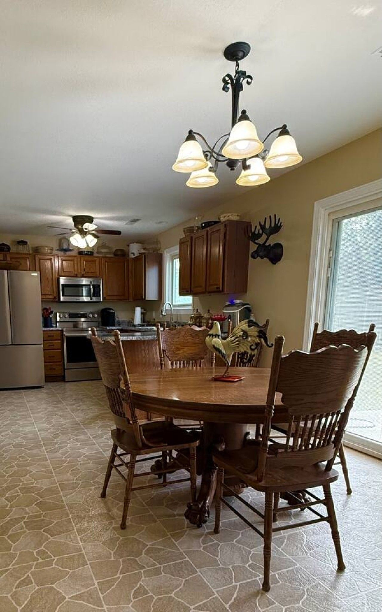 A kitchen with wooden cabinets, a dining table with chairs, a chandelier, and a refrigerator.