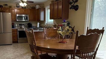 A kitchen with wooden cabinets, a dining table with chairs, a chandelier, and a refrigerator.