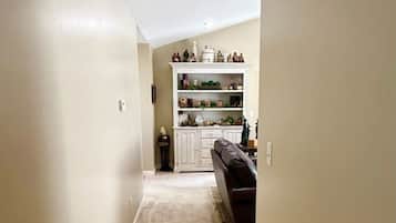 A narrow hallway with a carpeted floor leading to a room with a dark-colored sofa and a white cabinet with decorative items.