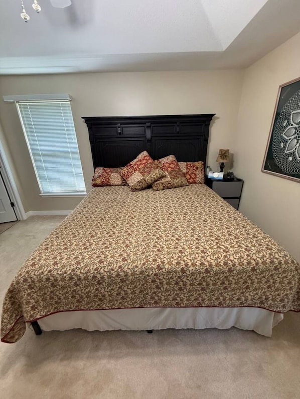 A bedroom with a large bed, a dark headboard, a window with blinds, and a framed artwork on the wall.