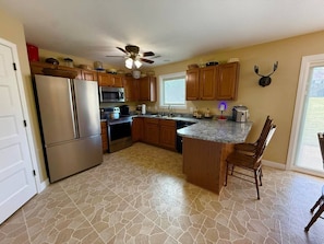 A kitchen with a central island, wooden cabinets, a refrigerator, microwave, and a ceiling fan.
