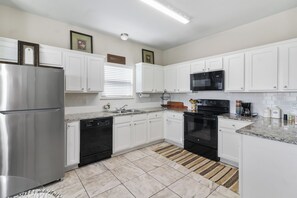 A modern kitchen with white cabinets, stainless steel appliances, and a patterned rug. - Furnished 3BR Home Near Baylor Scott & White, Monthly Stays (Temple)