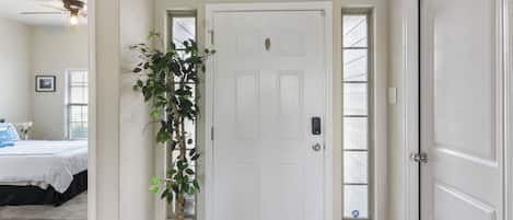 A hallway with a white door, a potted plant, and a window.