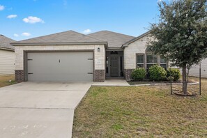 A two-story house with a garage, a front door, and a small front yard with a tree. - Furnished 3BR Home Near Baylor Scott & White, Monthly Stays (Temple)