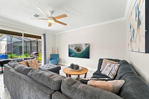 Ein modernes Wohnzimmer mit einem grauen Ecksofa, einem runden Couchtisch und einem Deckenventilator.