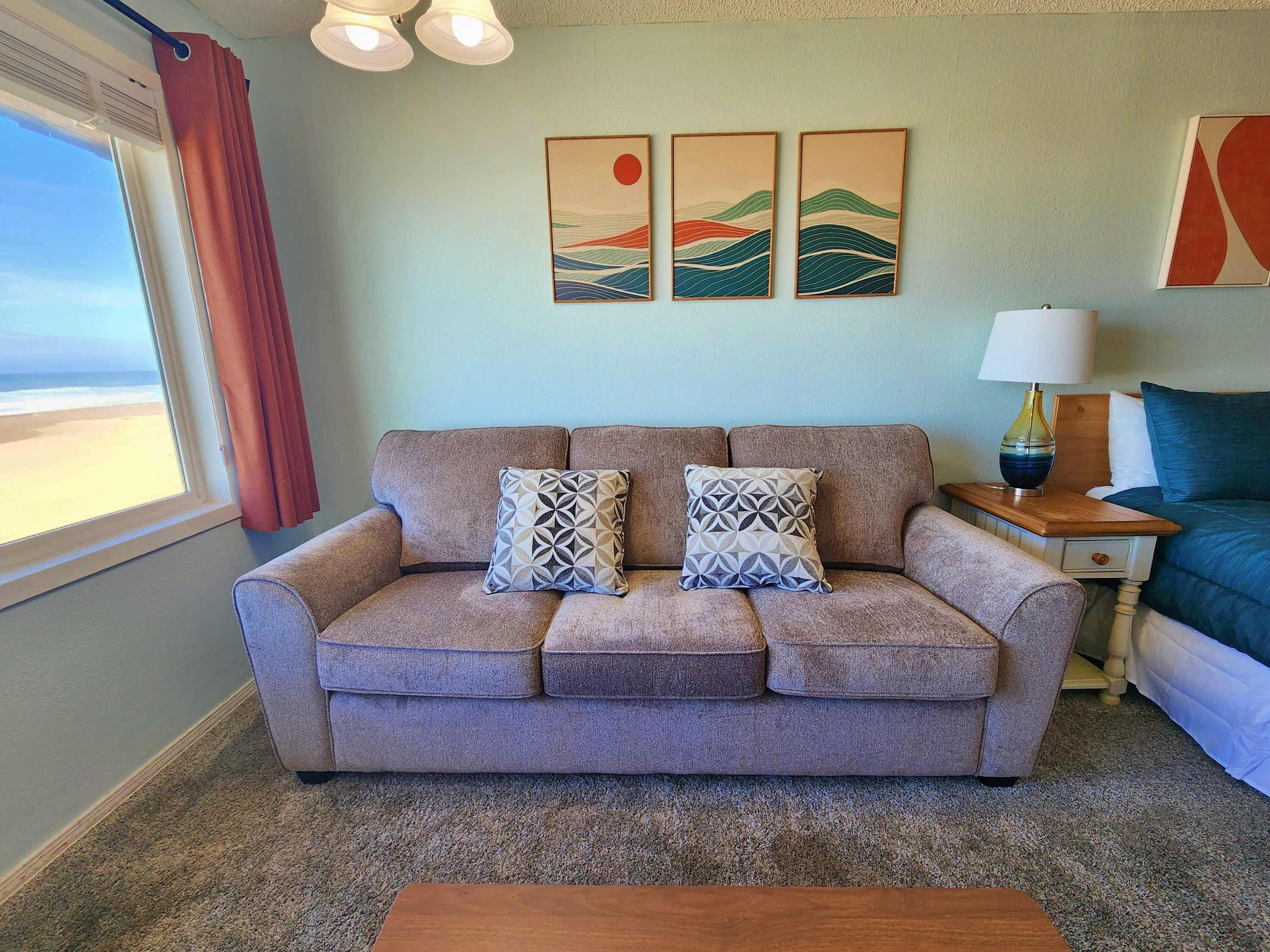 A living room with a sofa, two patterned pillows, a wooden coffee table, a lamp, and artwork on the wall.