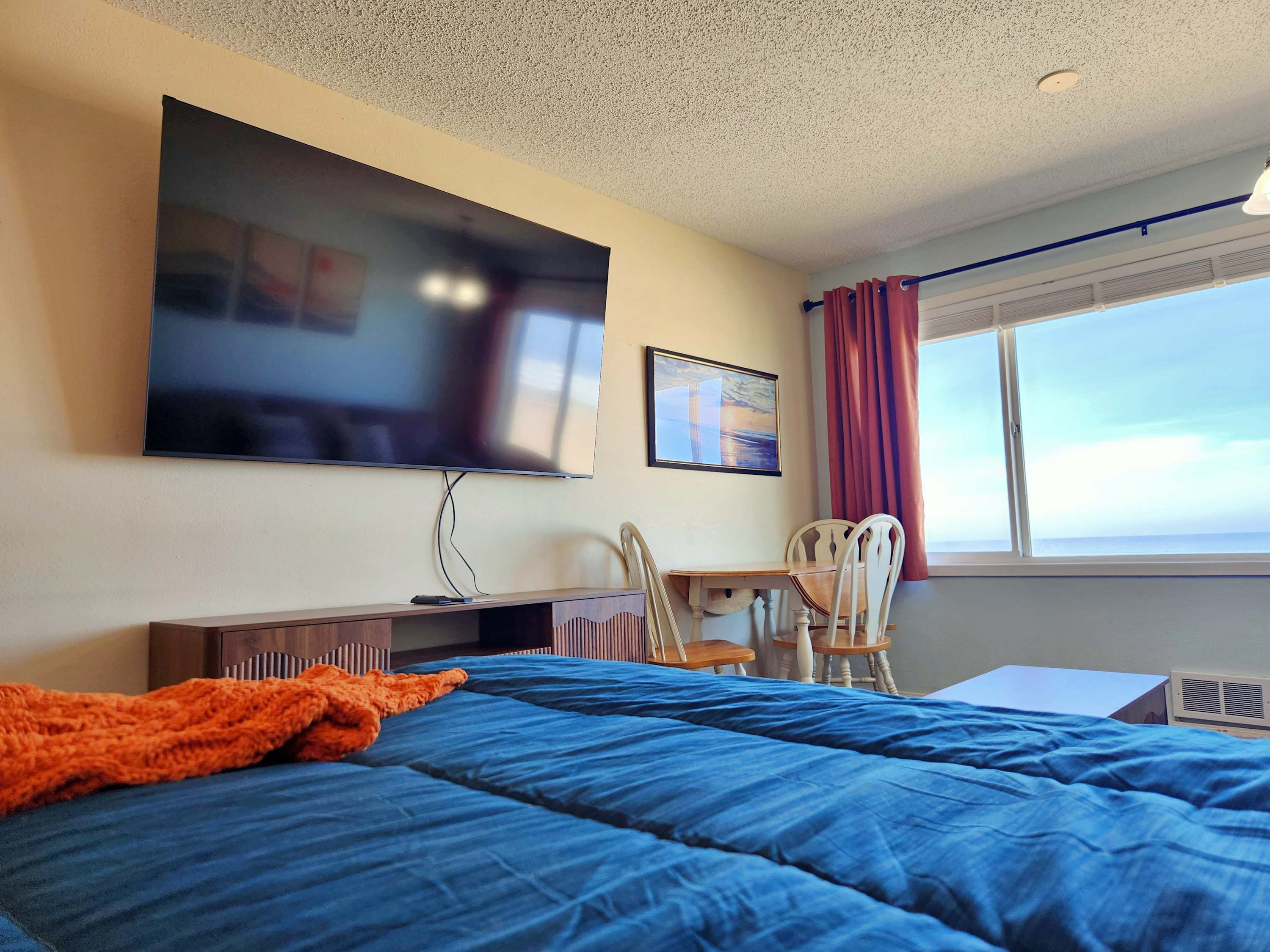 A bedroom with a bed, a desk, a chair, a television, and a window with curtains.