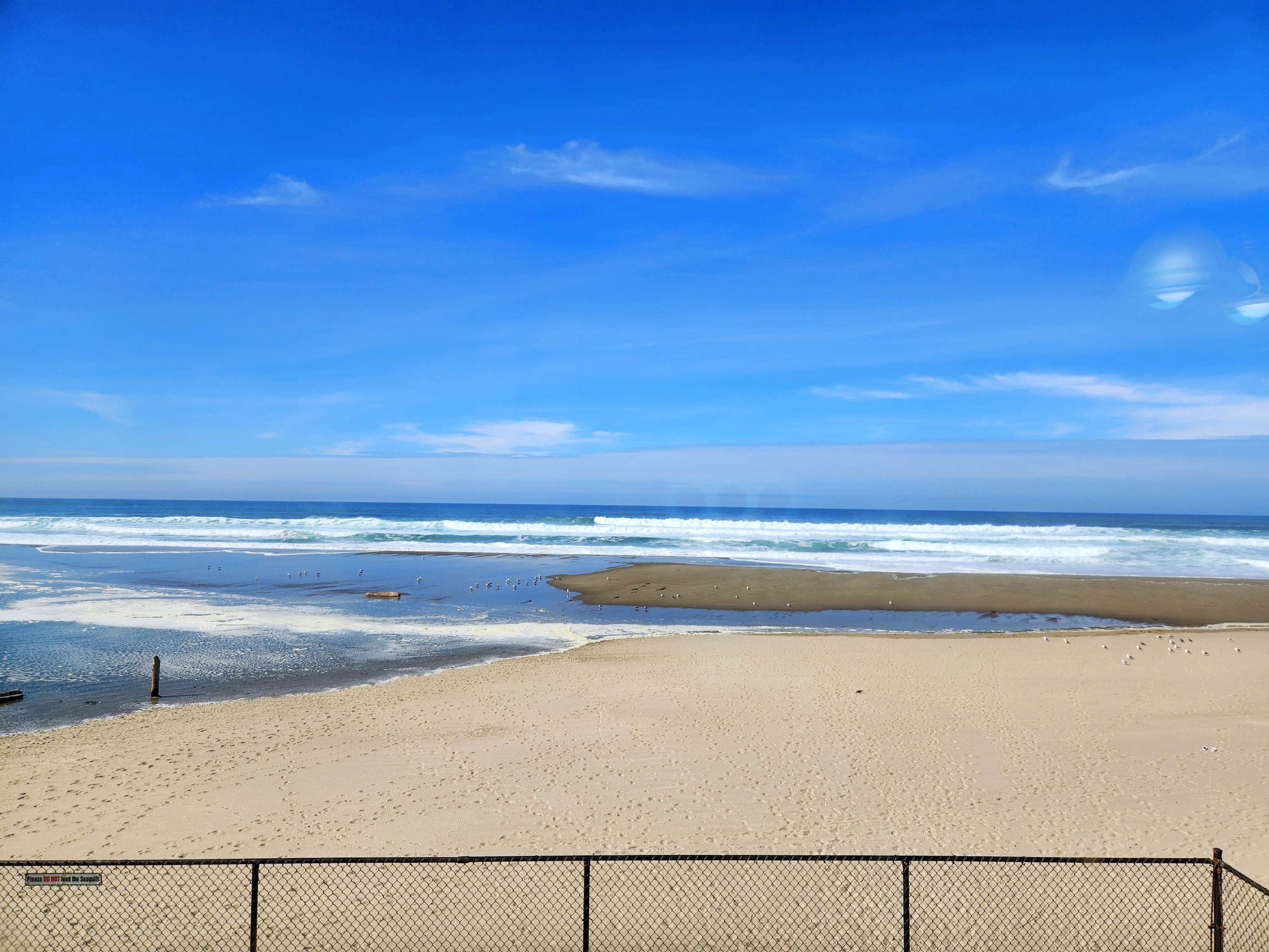 A beach with a fence in the foreground and waves in the background.