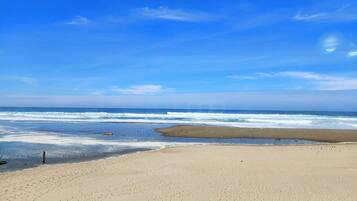 A beach with a fence in the foreground and waves in the background.