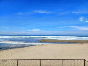 A beach with a fence in the foreground and waves in the background. - Oceanfront Condo With Kitchen, Pool, Hot Tub (Lincoln City)