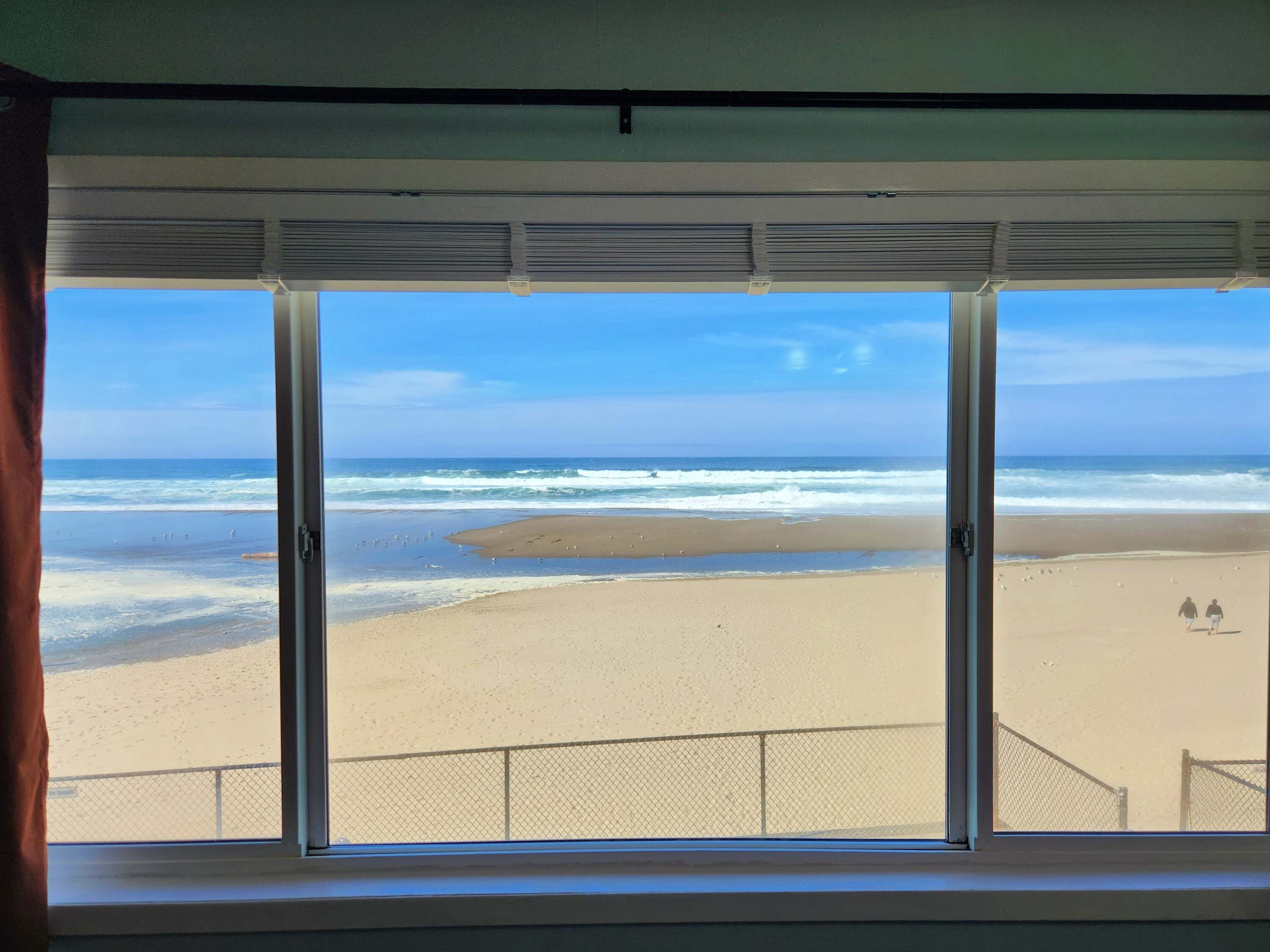 Una ventana con vistas a una playa, incluyendo el océano y una orilla arenosa.