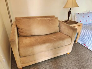 Ein beiges Sofa in einem Hotelzimmer mit einer Lampe und einem Bett mit einem gemusterten Bettbezug.
