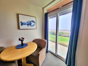 Ein Zimmer mit Tisch, Stuhl, einem gerahmten Bild und einem großen Fenster mit Vorhängen.