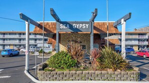 Ein Hotel Eingang mit einem Schild mit der Aufschrift 'SEA GYPSY', einer Steinfassade und einem Parkplatz mit Autos.