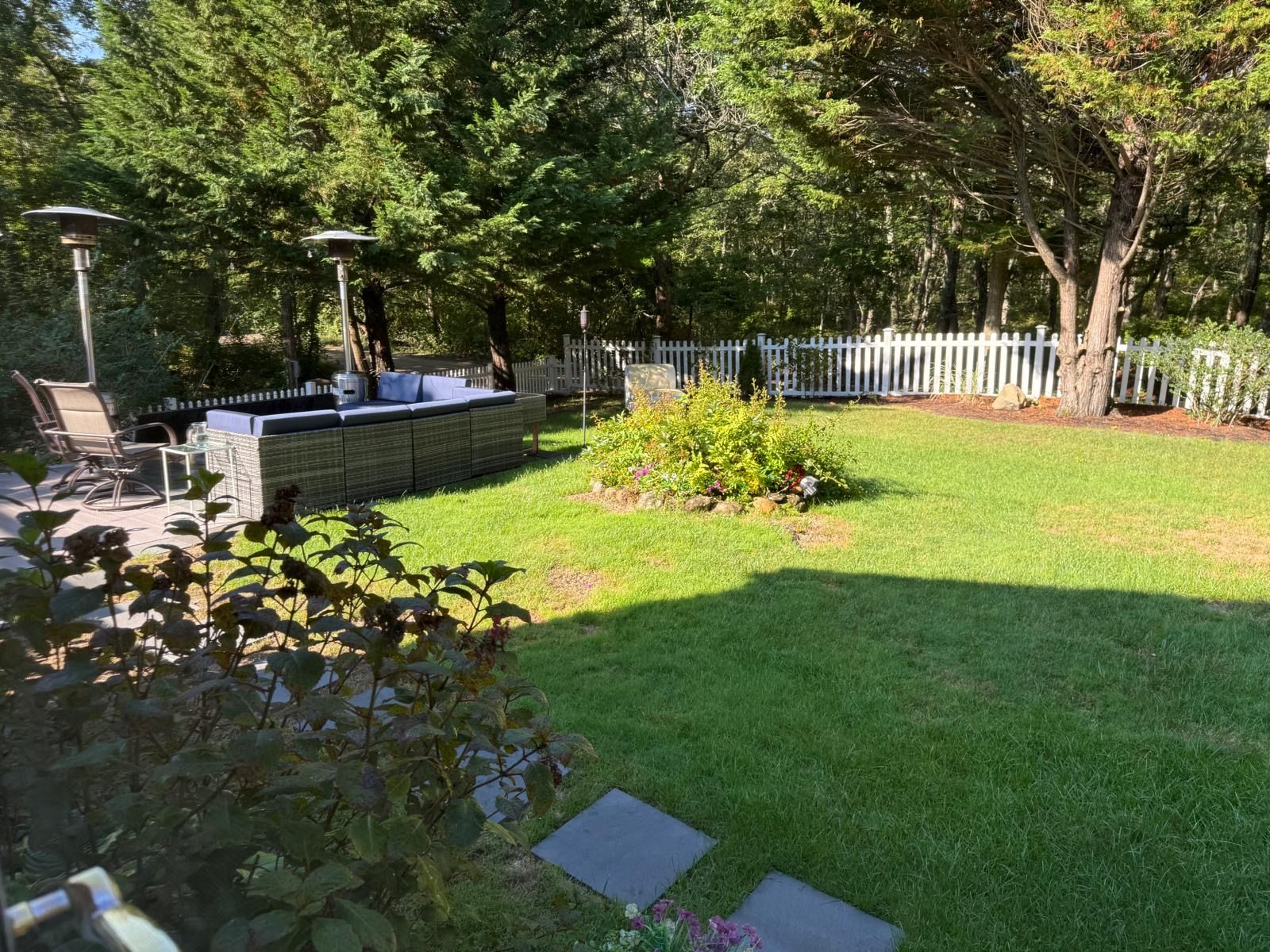 A backyard with a seating area, a white fence, and a variety of plants.