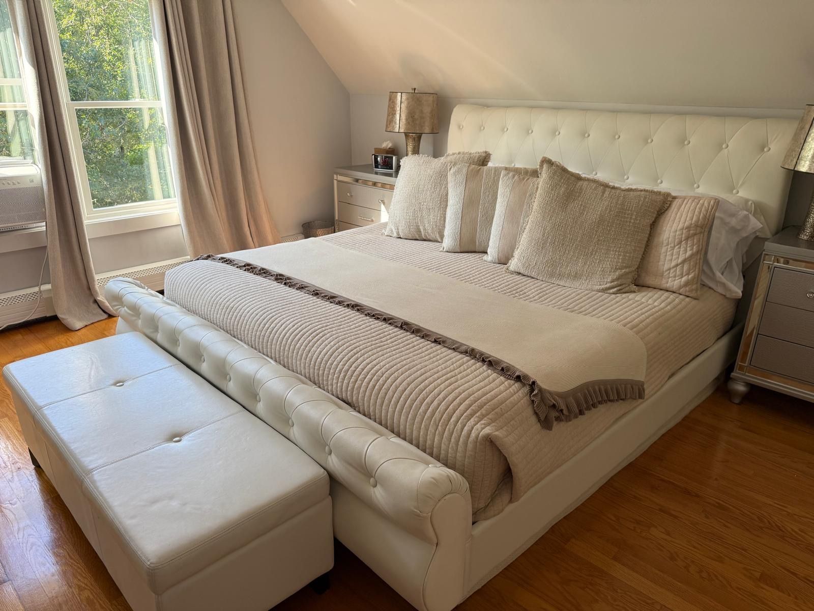 Une chambre à coucher avec un grand lit, une table de chevet, une lampe et une fenêtre avec des rideaux.