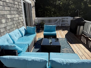 A deck with a sofa, two side tables, and a grill.