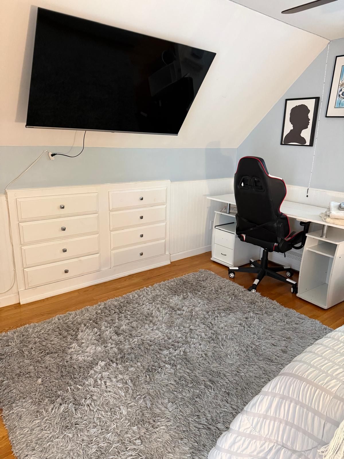 Een slaapkamer met een bed, een bureau, een stoel, een aan de muur bevestigde televisie en een dressoir.