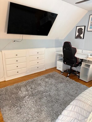 Een slaapkamer met een bed, een bureau, een stoel, een aan de muur bevestigde televisie en een dressoir.