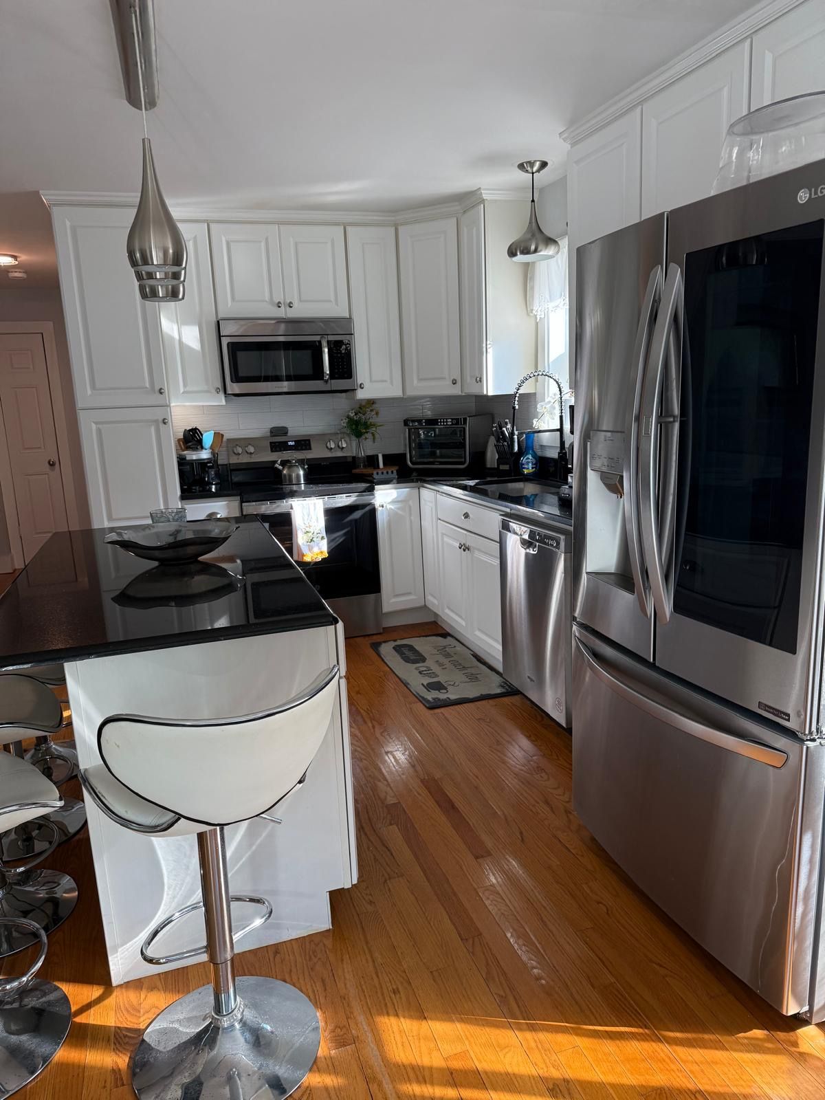 Una cocina moderna con electrodomésticos de acero inoxidable, armarios blancos y un taburete de bar.