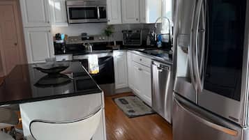 Una cocina moderna con electrodomésticos de acero inoxidable, armarios blancos y un taburete de bar.