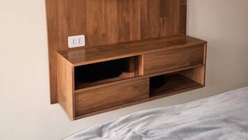 A wooden entertainment unit with a flat-screen TV mounted above it, a power outlet, and a lower shelf with drawers.