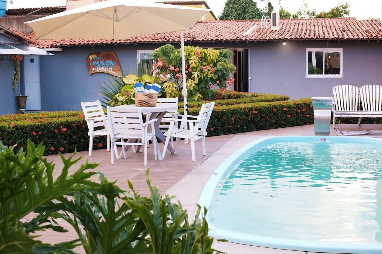 Un área junto a la piscina con mesa y sillas, una piscina pequeña y un edificio con un letrero.