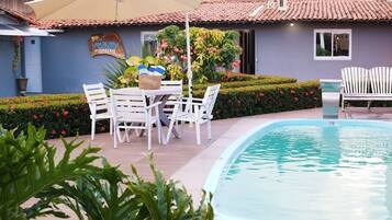 Un área junto a la piscina con mesa y sillas, una piscina pequeña y un edificio con un letrero.