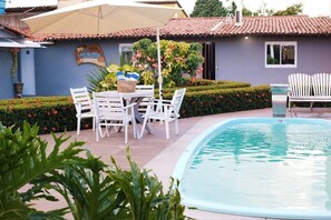 A poolside area with a table and chairs, a small pool, and a building with a sign.