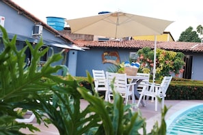 A poolside area with a table and chairs, a water tank, and a building with a sign. - Dai Costa - Casa de Praia (Tamandaré)