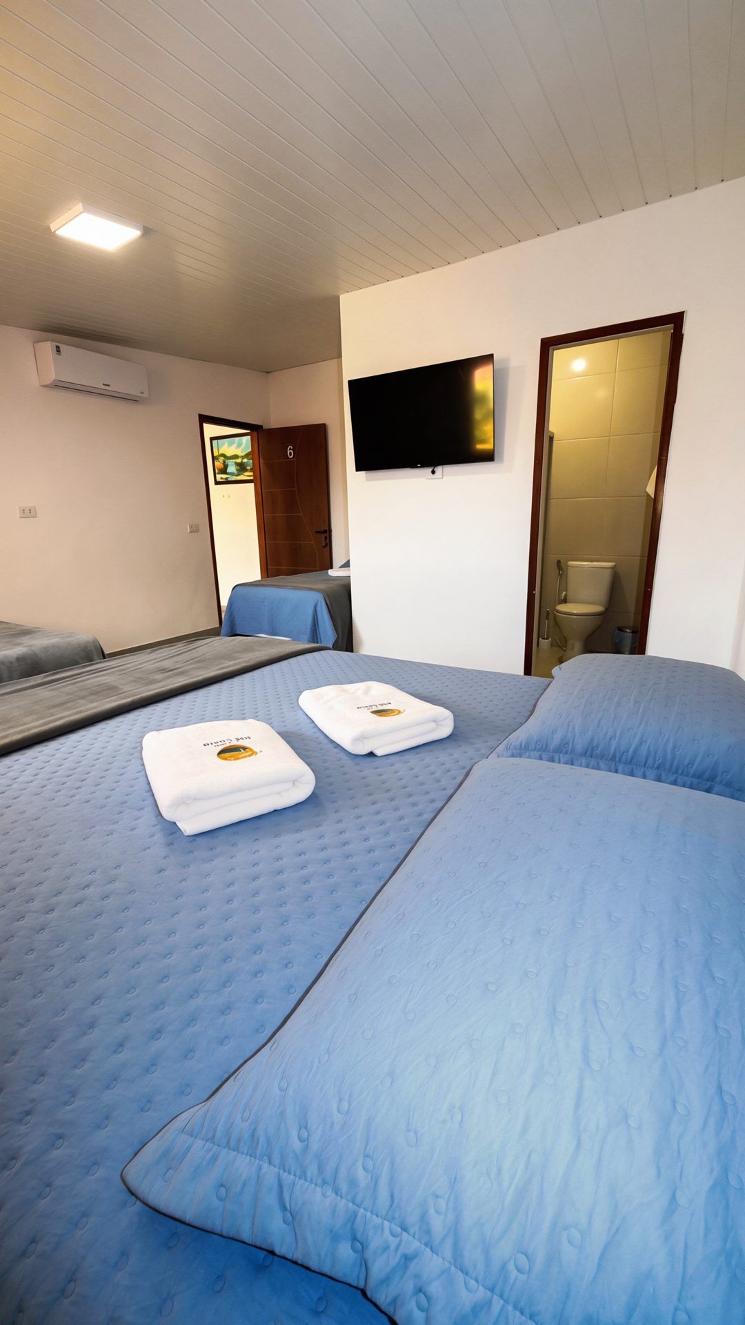Habitación de hotel con dos camas, un televisor de pantalla plana montado en la pared y un área de ducha visible a través de una puerta abierta.