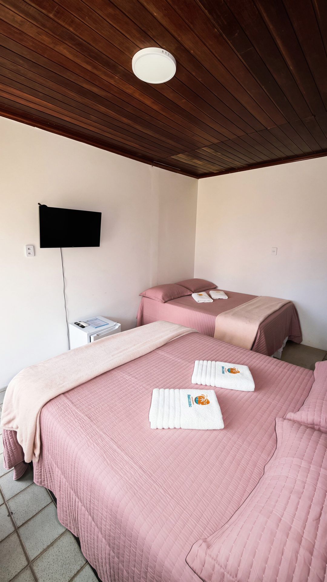 A hotel room with two beds, a flat-screen TV, a bedside table, and a ceiling light.