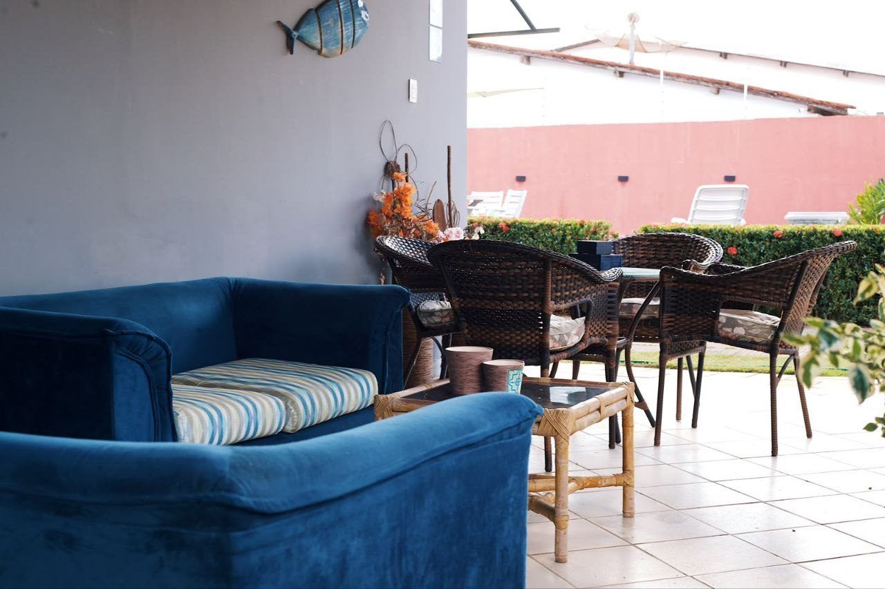 Un sofá azul con un cojín a rayas, una mesa de comedor de mimbre con sillas y un adorno en la pared.