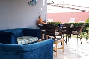 Un sofá azul con un cojín a rayas, una mesa de comedor de mimbre con sillas y un adorno en la pared.