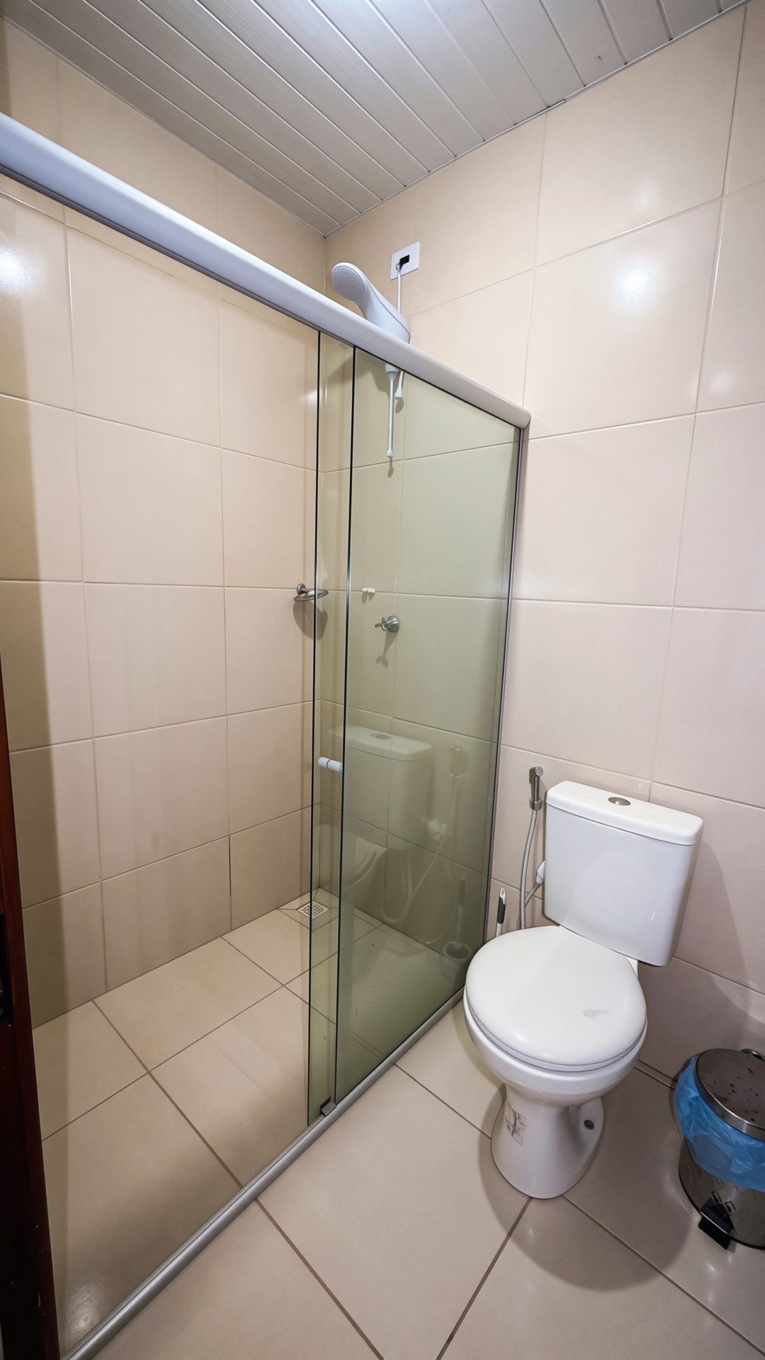 A bathroom with a glass-enclosed shower, a toilet, and a blue trash bin.