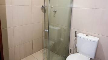 A bathroom with a glass-enclosed shower, a toilet, and a blue trash bin.