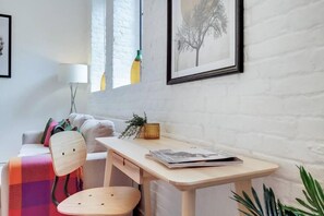 Un salon moderne avec un mur en briques blanches, un bureau en bois, un canapé, un fauteuil et un lampadaire.