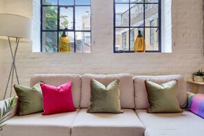 A room with a sofa, pillows, a lamp, and a window with a view of buildings. - VY6 - Stylish 1-Bed Flat Near Borough (London)