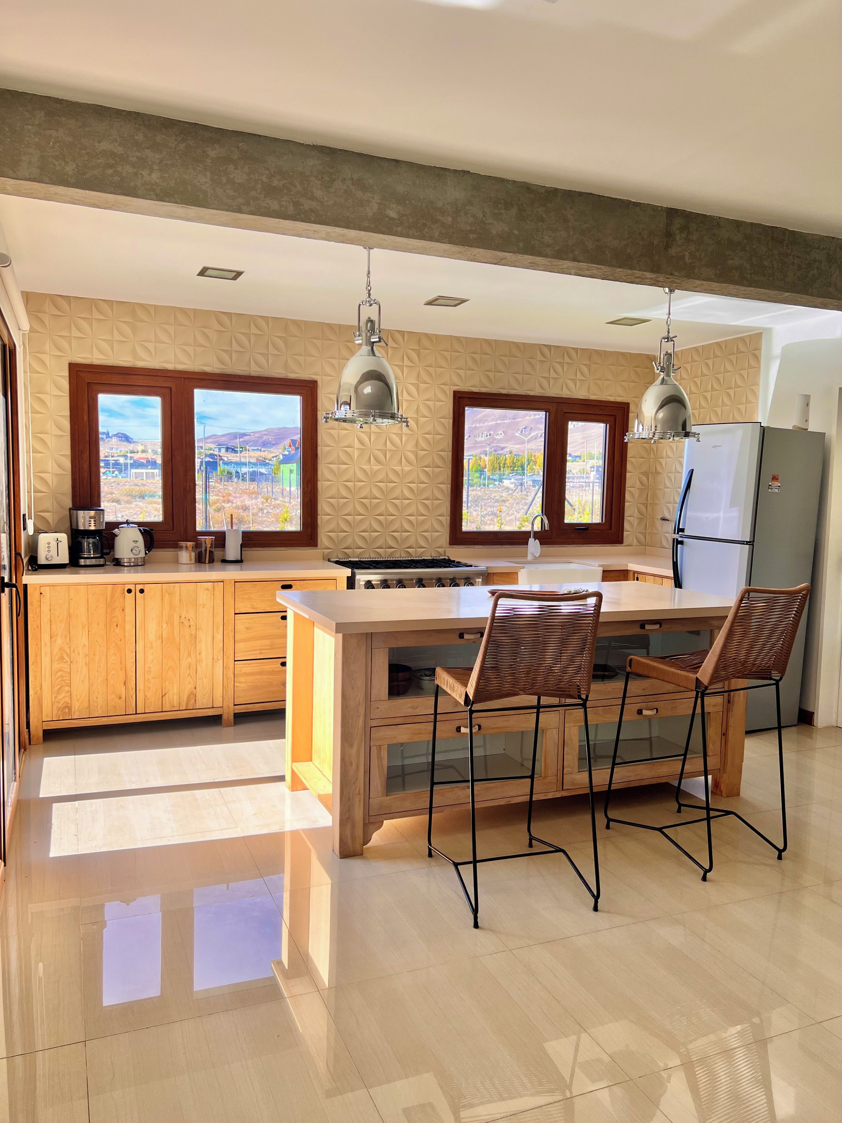 Une cuisine moderne dotée d’un îlot central, de meubles en bois et de deux fenêtres donnant sur un paysage.