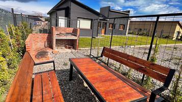 An outdoor seating area with a wooden bench and table, surrounded by gravel and a metal fence.