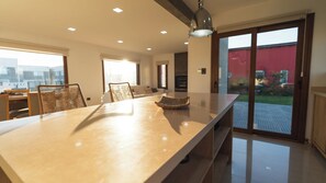 A modern kitchen with a large island, dining chairs, and a view of the outdoors.