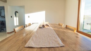A long dining table with six chairs, a wooden floor, and a large window providing natural light.