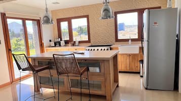 Une cuisine moderne dotée d’un îlot central, de tabourets de bar, d’un réfrigérateur et de grandes fenêtres offrant une vue dégagée.