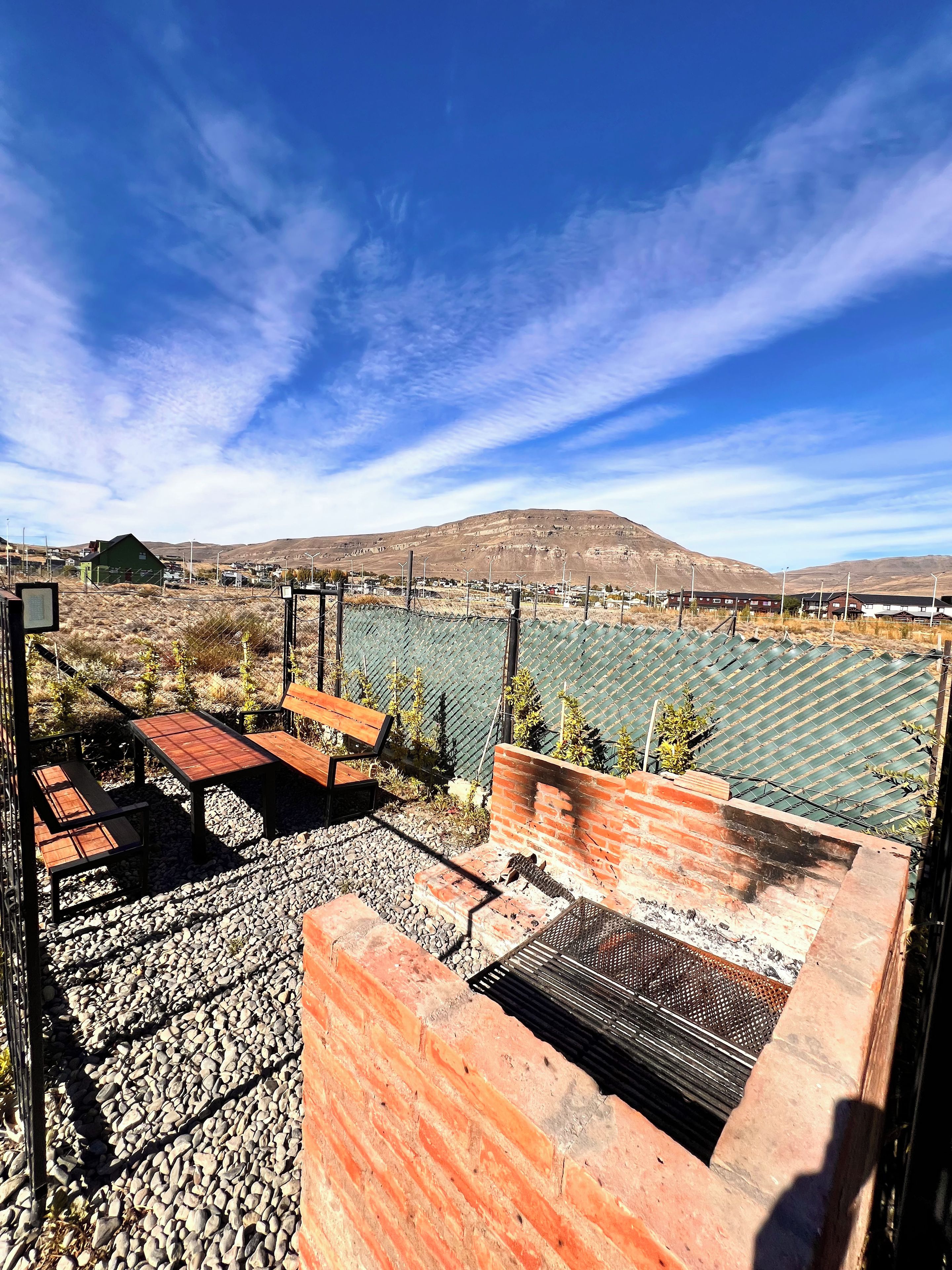 A rooftop patio with a view of a mountainous landscape, outdoor seating, and a metal grill.
