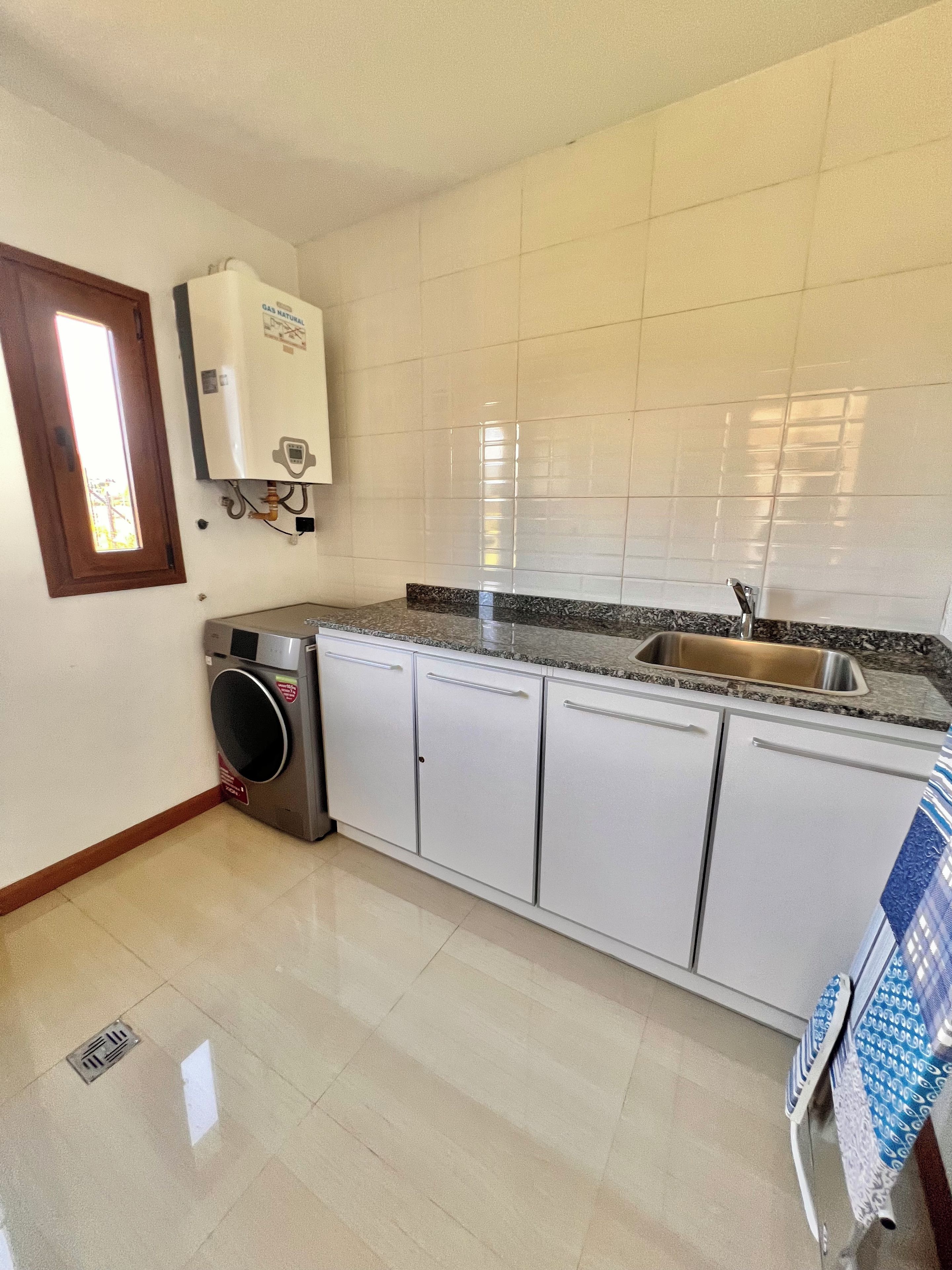 Una cocina con armarios blancos, un lavamanos de acero inoxidable, lavadora incorporada y una ventana con vistas.
